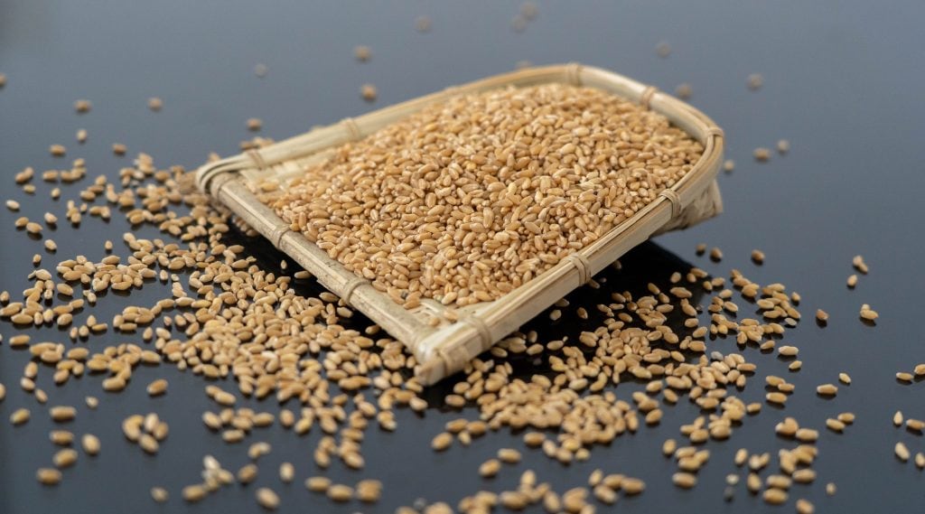 Sesame seeds in a woven basket with some scattered around on a dark surface.